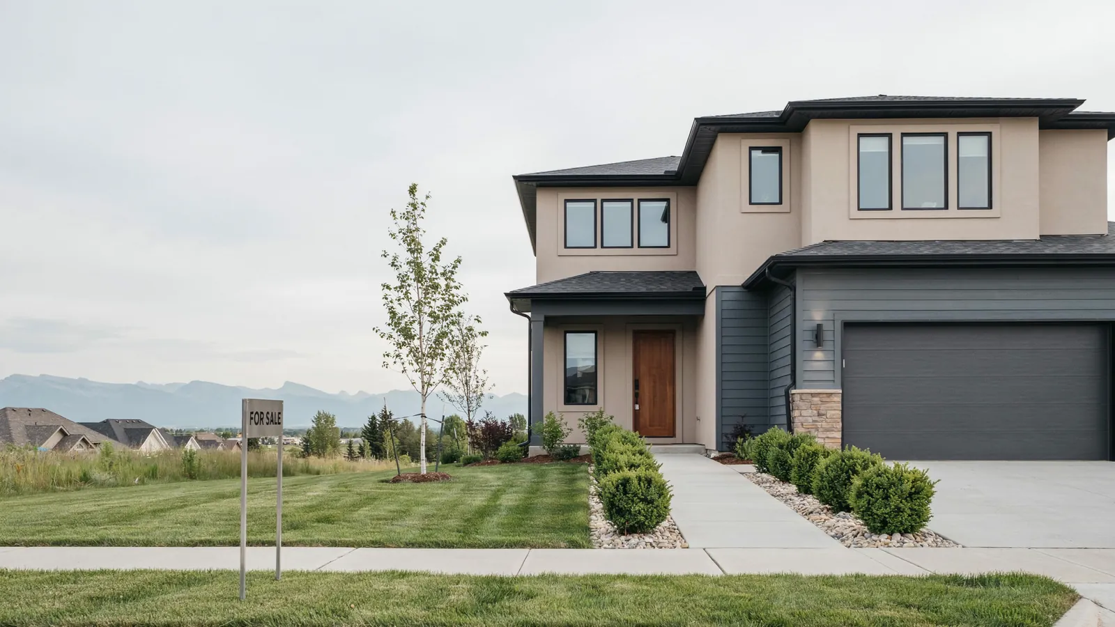 A modern two storey home with mountains behind it and a for sale sign on the lawn, the Cochrane foreclosure guide